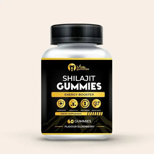 A white bottle of "Mister Gummies" Shilajit Gummies sits on a light pink surface. The black label has gold accents and lists the product as an "Energy Booster." Icons below the text highlight its benefits for immune support, performance and stamina, anti-aging, and sexual health. The bottle contains 60 gummies and is an elderberry flavor.