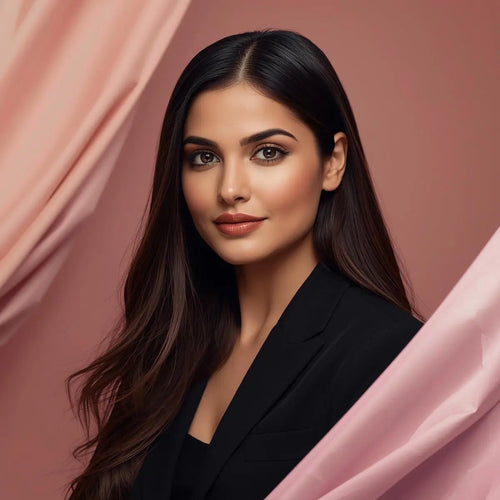 Studio portrait of a young woman with long dark hair, wearing a black blazer, with a soft, natural makeup look, framed by flowing pink fabric.